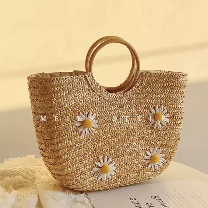 Bolsa artesanal de palha premium Lavinni Margarida Bali com aplicações florais e alças circulares de madeira sob luz natural.