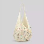 Visão em ângulo semi-lateral da bolsa de crochê de praia Lavinni Capri Pearl branca, destacando a trama vazada e o brilho das contas peroladas coloridas.
