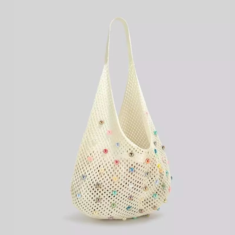 Visão em ângulo semi-lateral da bolsa de crochê de praia Lavinni Capri Pearl branca, destacando a trama vazada e o brilho das contas peroladas coloridas.