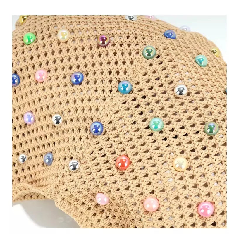 Close-up da bolsa de praia chique Lavinni Capri Pearl em tom cáqui, destacando a textura tricotada da malha vazada e a aplicação das pérolas coloridas.