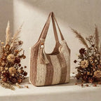 Bolsa de praia chique Lavinni Sunset Stripes em tom marrom e bege posicionada em estúdio entre arranjos decorativos de flores secas.