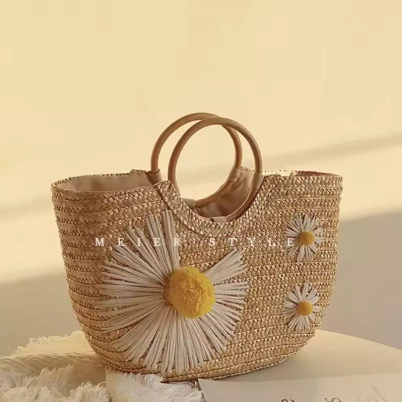 Bolsa de praia de palha Lavinni Margarida Bali em ângulo diagonal destacando a grande flor de margarida com pompom amarelo tridimensional.