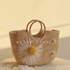 Bolsa de praia de palha Lavinni Margarida Bali em ângulo diagonal destacando a grande flor de margarida com pompom amarelo tridimensional.