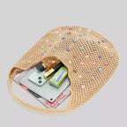 Visão interna da bolsa de praia grande Lavinni Capri Pearl com pertences organizados, mostrando smartphone, perfume, batom e revista no compartimento principal.