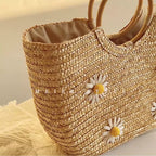 Visão lateral em ângulo detalhando a trama de palha natural e as pequenas flores de margarida aplicadas na bolsa de praia Lavinni Margarida Bali.