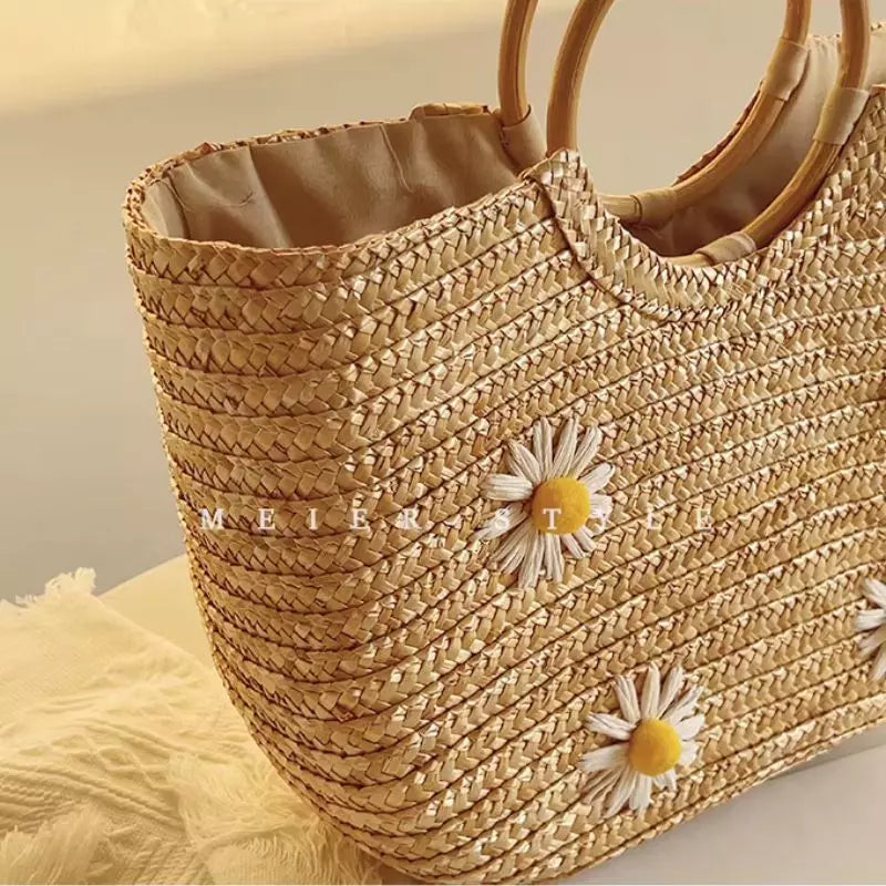 Visão lateral em ângulo detalhando a trama de palha natural e as pequenas flores de margarida aplicadas na bolsa de praia Lavinni Margarida Bali.